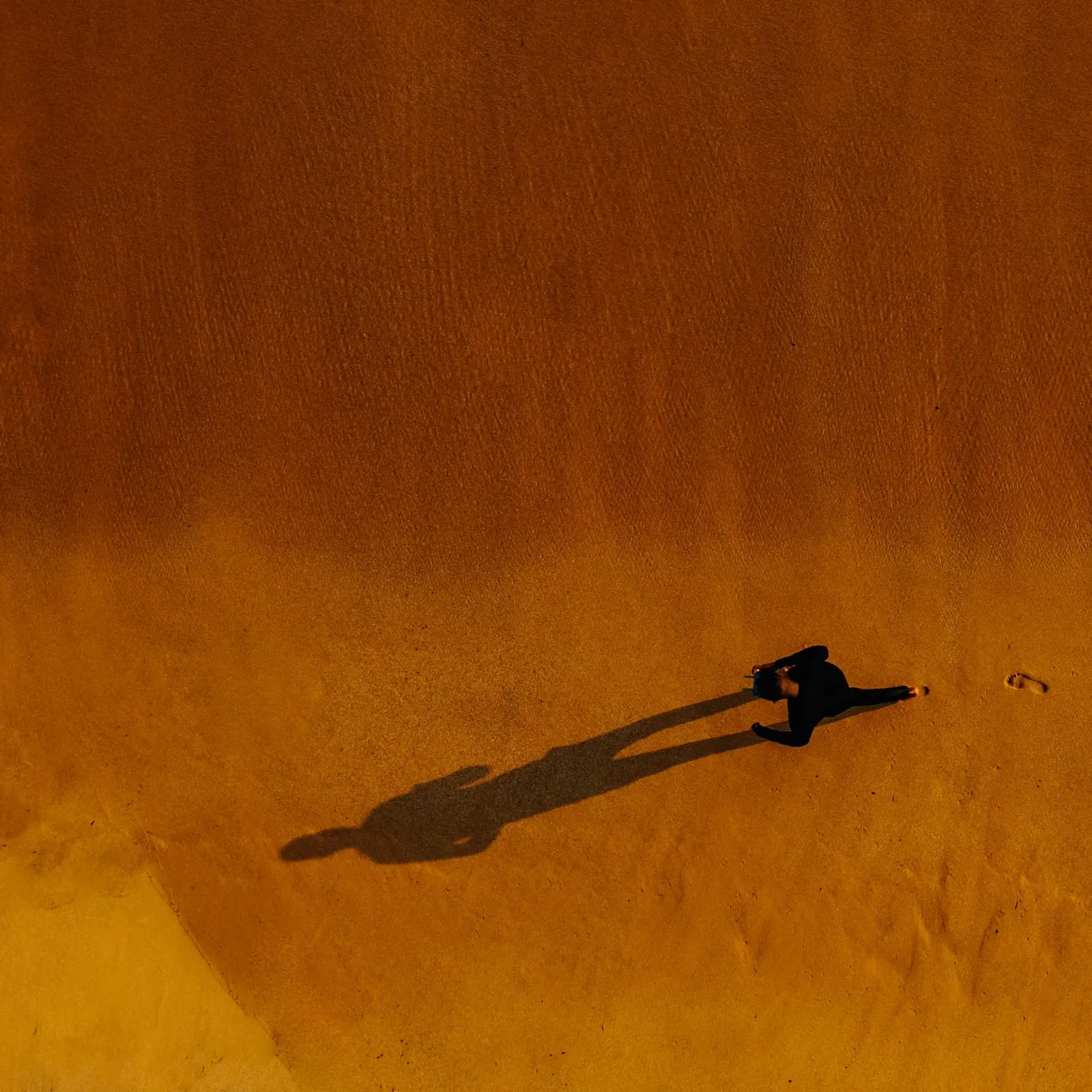 A lone person standing on open sand, casting a long shadow